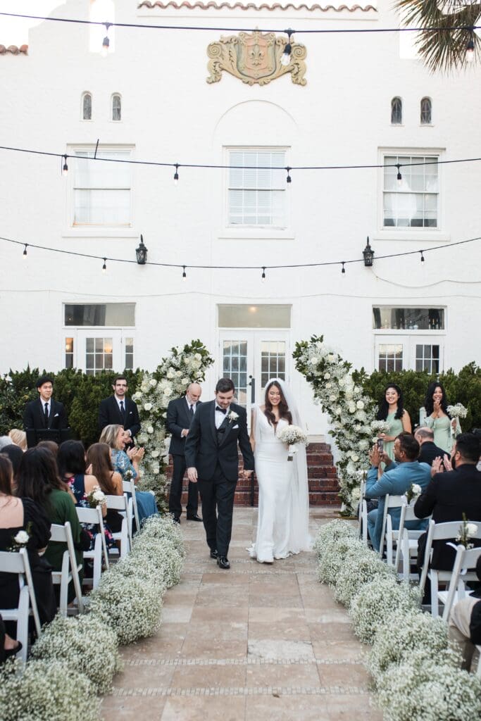 Bride and groom walking down the aisle after their ceremony at Casa Marina Hotel in Jacksonville, Florida, surrounded by guests and white florals. | Jacksonville Wedding Photography